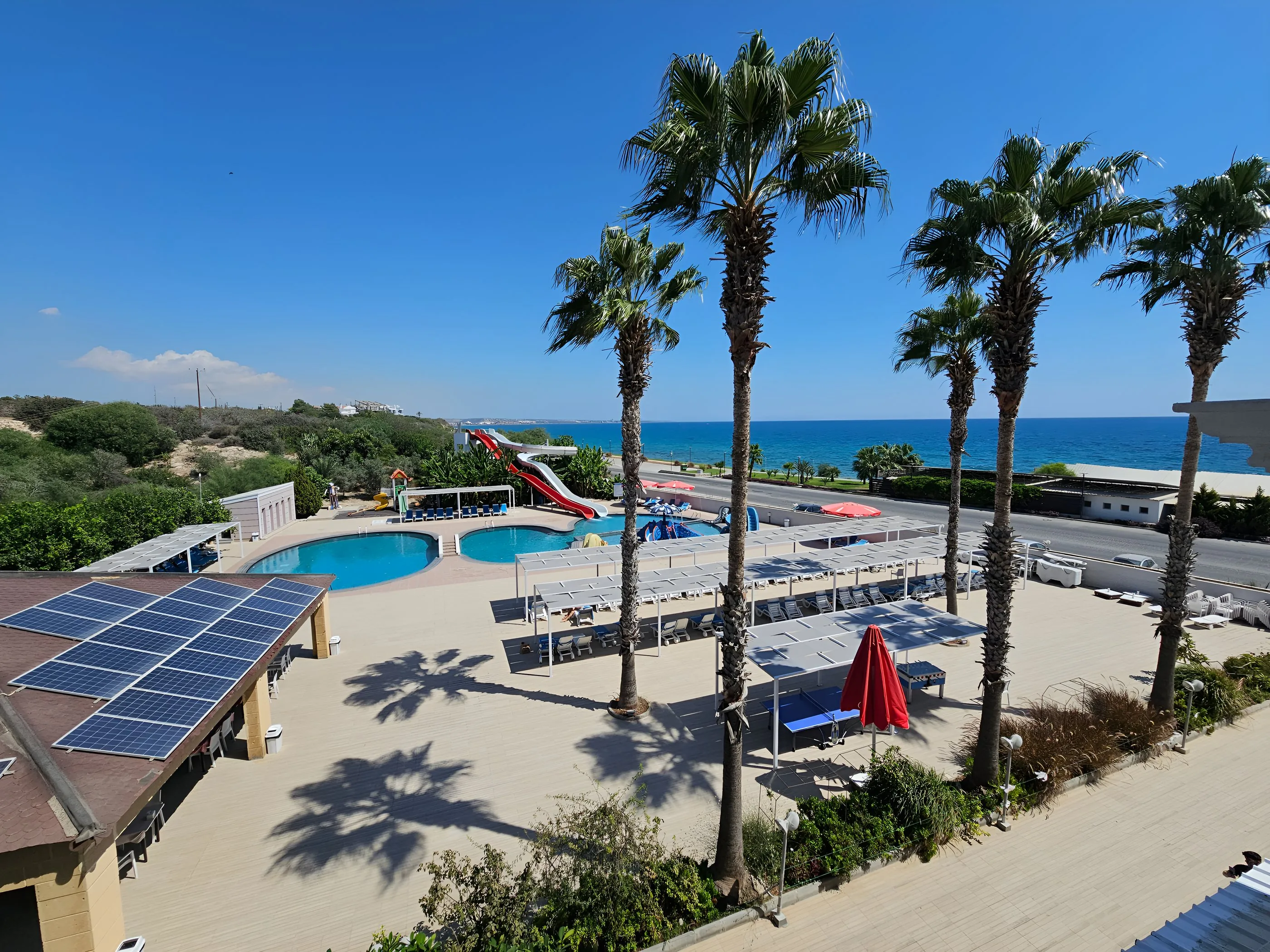 Exotic Hotel pool with red and white water slides, palm trees and the sea behind